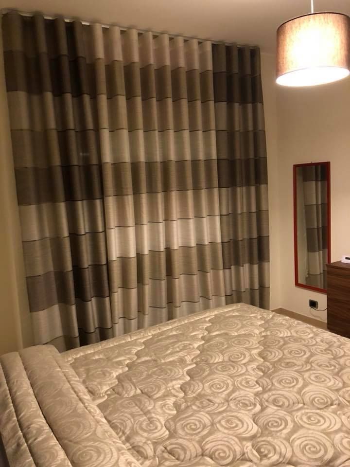 Camera da letto con tende a righe, copriletto a fantasia e lampada da parete accanto a uno specchio.