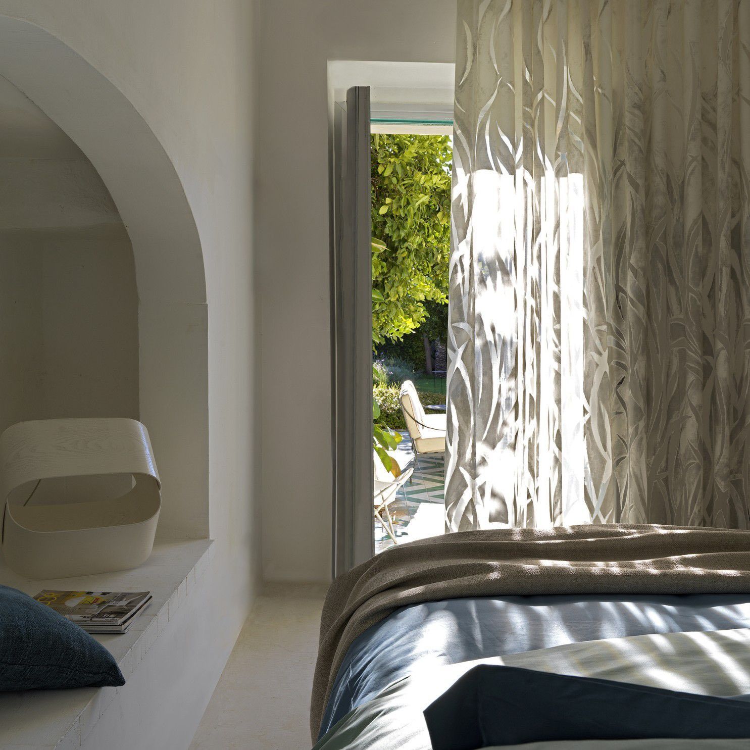 Luminosa camera da letto con alcova ad arco, letto e finestra aperta che si affaccia su un giardino soleggiato.