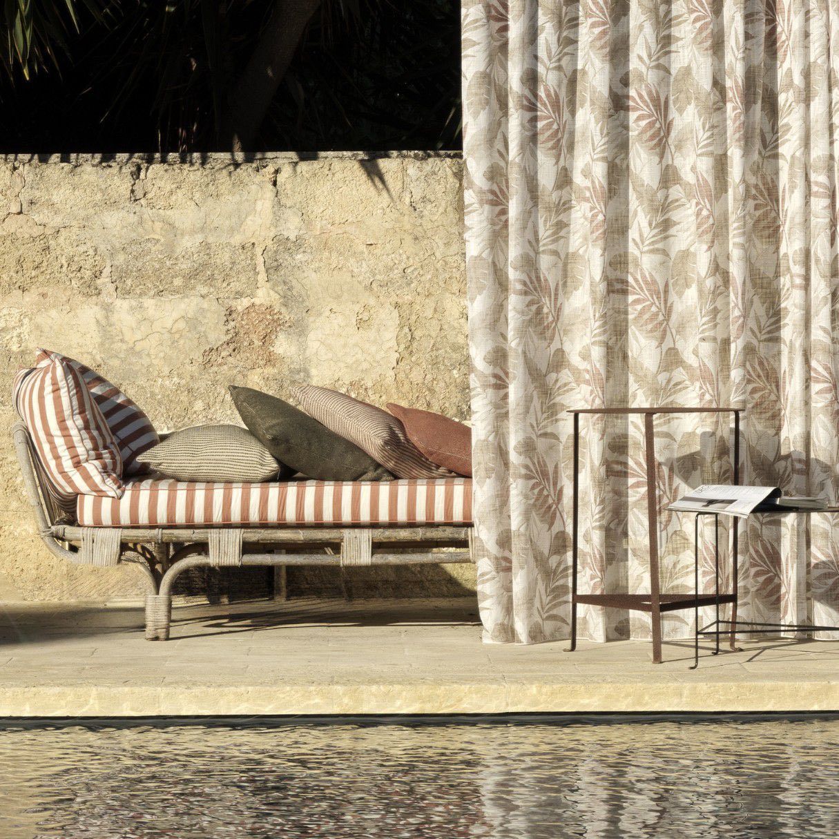 Una chaise longue a righe accanto a una tenda e un tavolino su un patio soleggiato a bordo piscina.