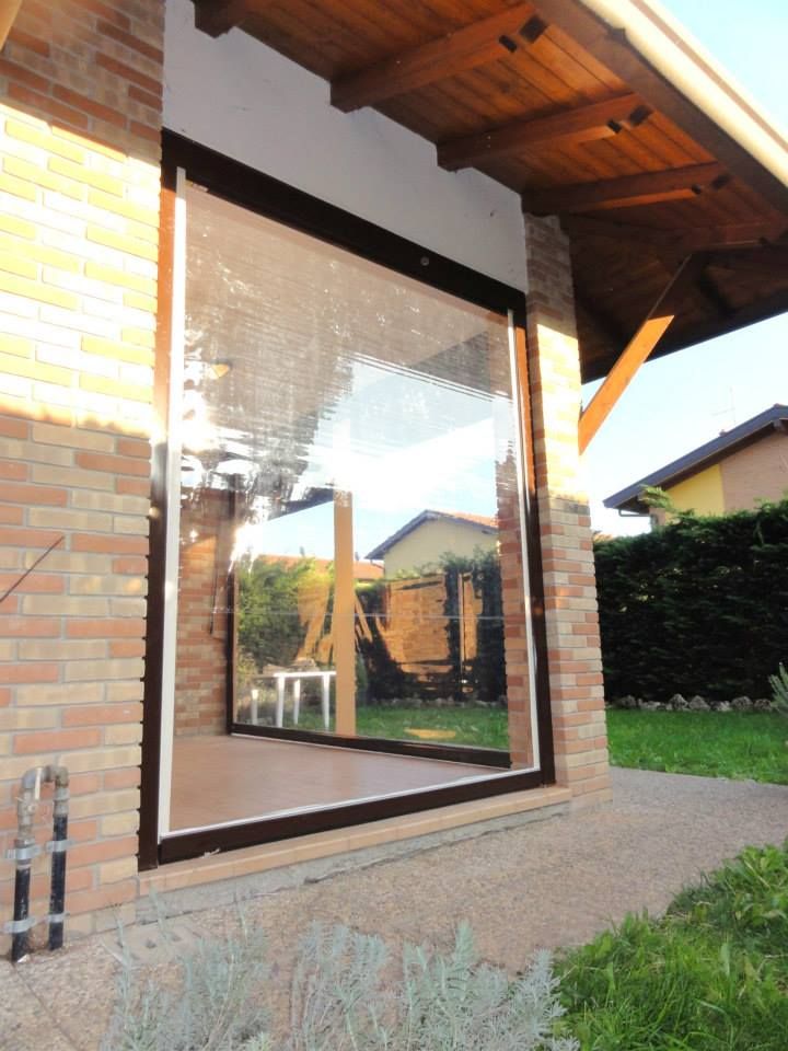 Porta scorrevole in vetro su una casa in mattoni, che riflette un giardino e la sporgenza del tetto in legno.