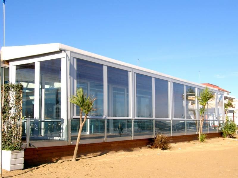 Moderno edificio in vetro su un lotto sabbioso sotto un cielo azzurro limpido.