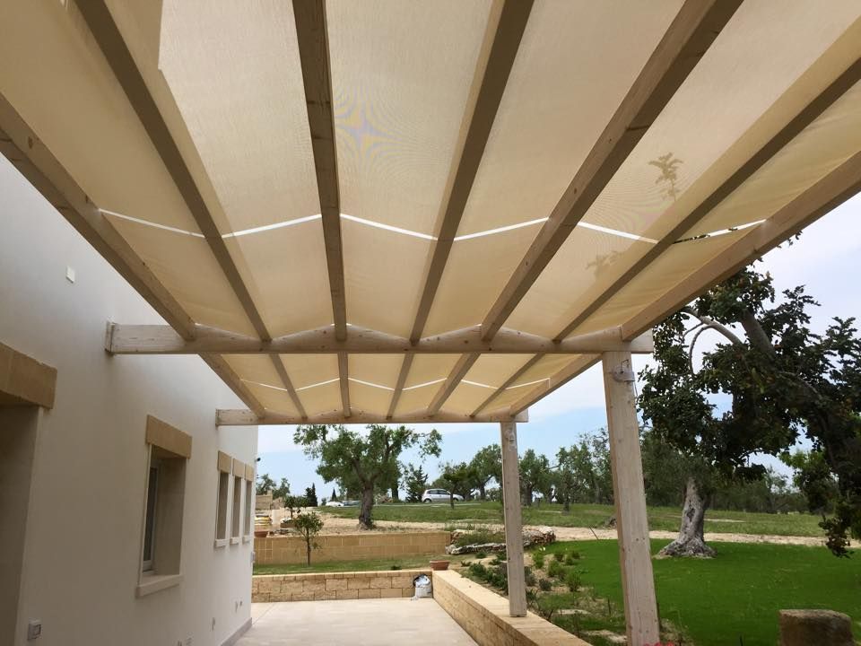 Patio coperto con travi a baldacchino beige che si affaccia su un prato verde e sugli alberi.