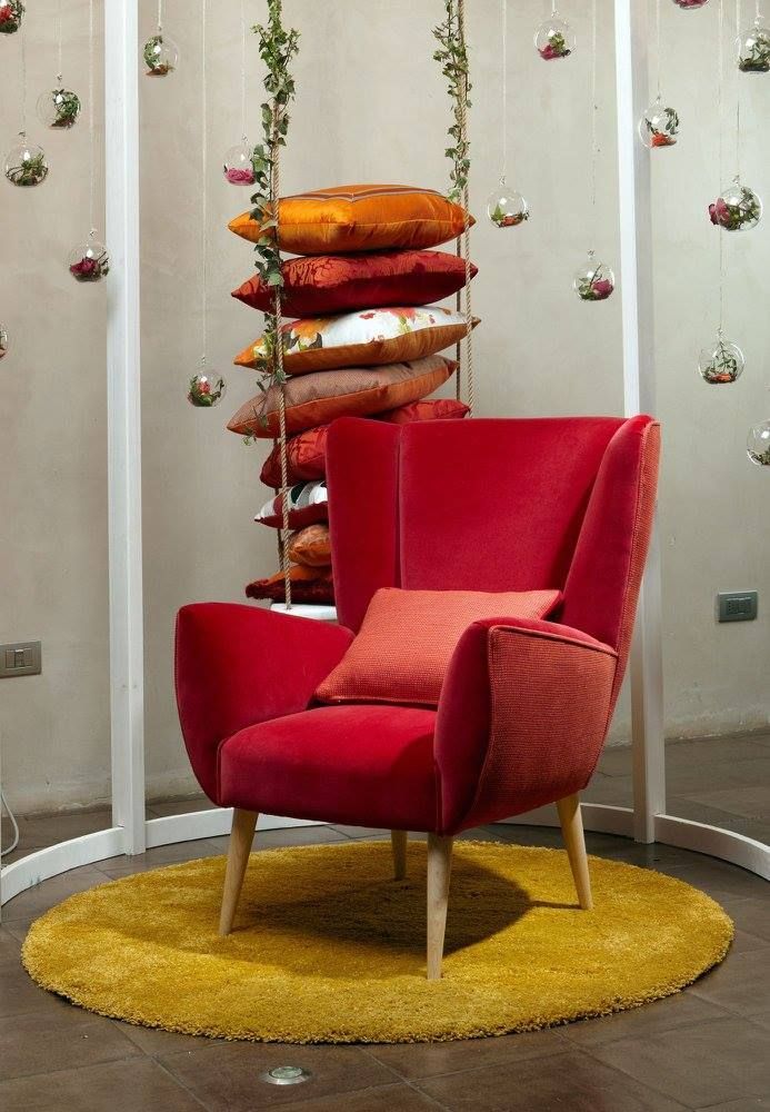 In una stanza decorata, una poltrona imbottita di colore rosso è appoggiata su un tappeto giallo, accanto a una pila di cuscini.