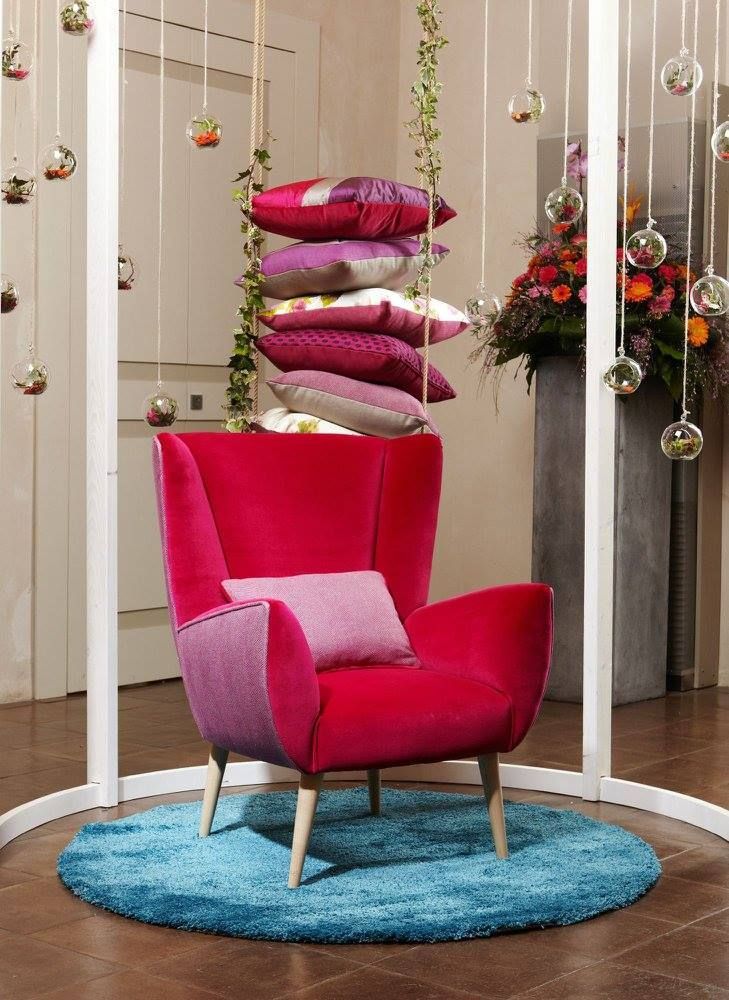 Poltrona rosa acceso con cuscini decorativi su un tappeto blu in uno showroom arredato con gusto.