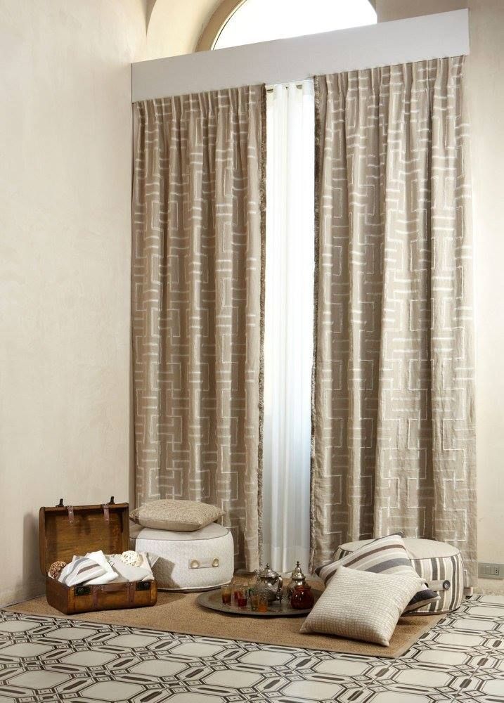 Tende beige che incorniciano una finestra luminosa con cuscini e cesti intrecciati su un tappeto.