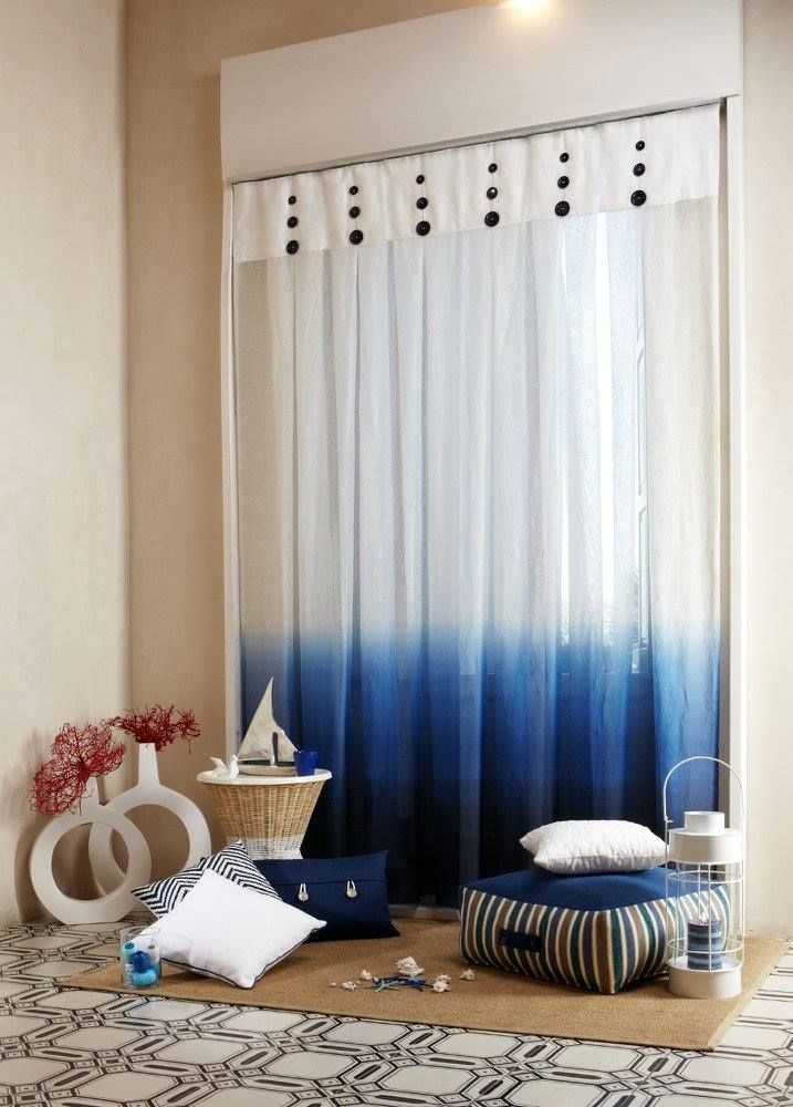 Accogliente angolo soggiorno con tende sfumate di blu, cuscini da pavimento, decorazioni e un tavolino con cestino.