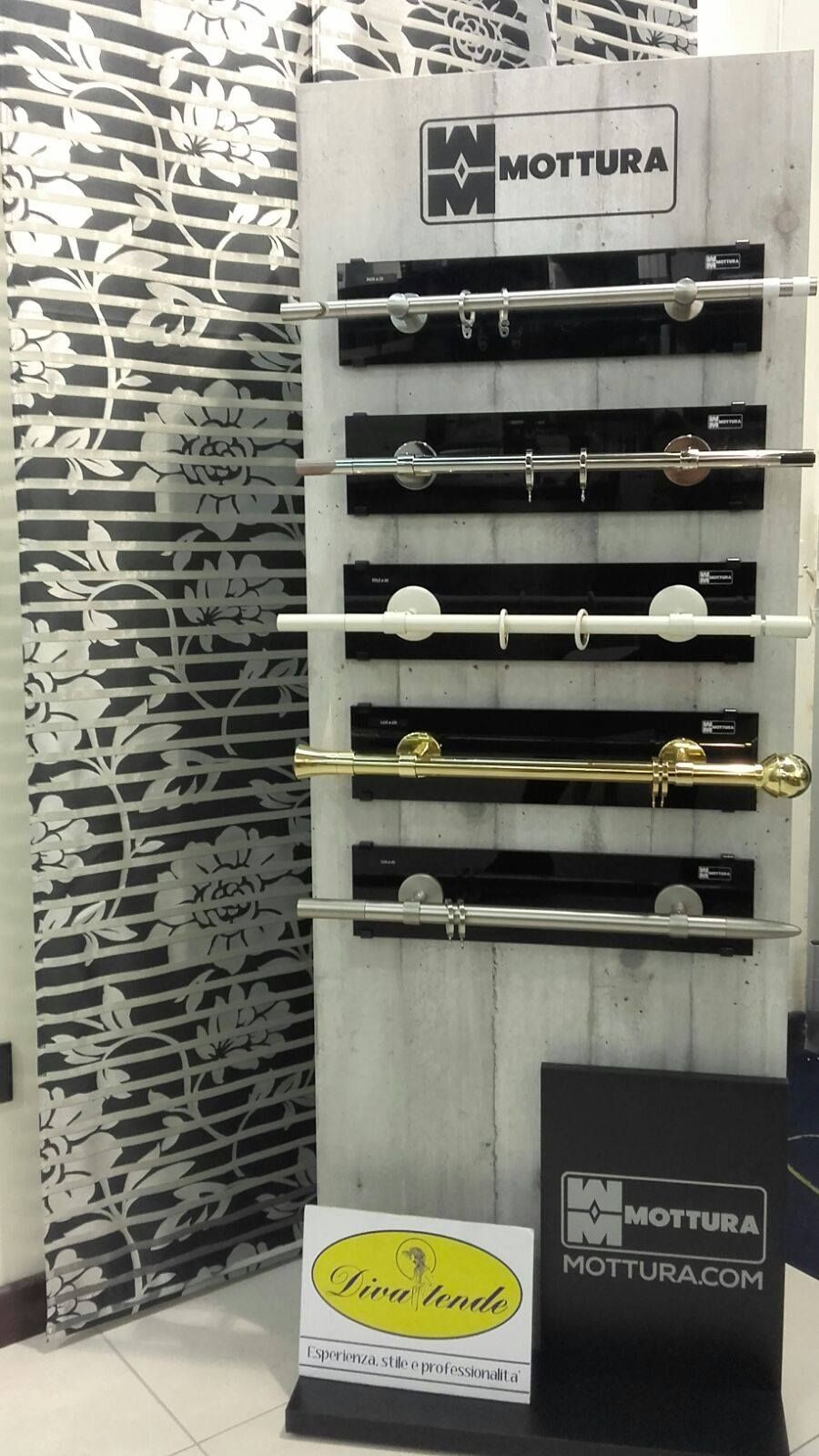 Esposizione di bastoni e terminali decorativi in metallo per tende in uno showroom, con uno sfondo a parete decorato.