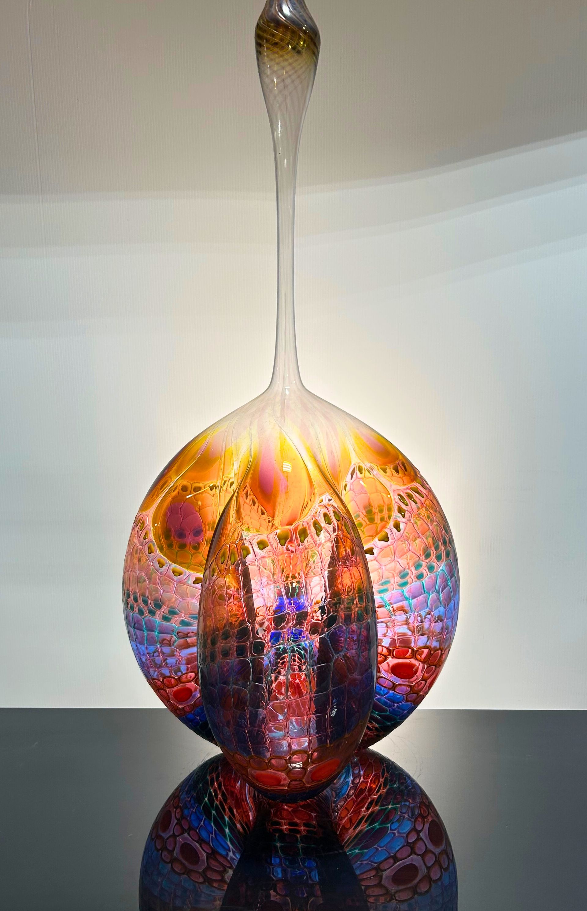 Glass sculpture with spherical body, long neck, and iridescent colors.