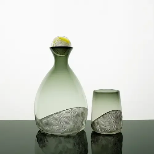 Green glass decanter with stopper and matching tumbler, both with etched base detail, on black surface.