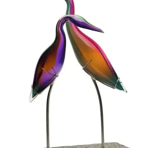 Glass art sculpture of two colorful birds with curved necks, perched on metal legs.