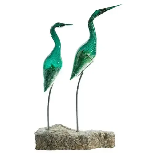 Two teal glass heron sculptures on a stone base.