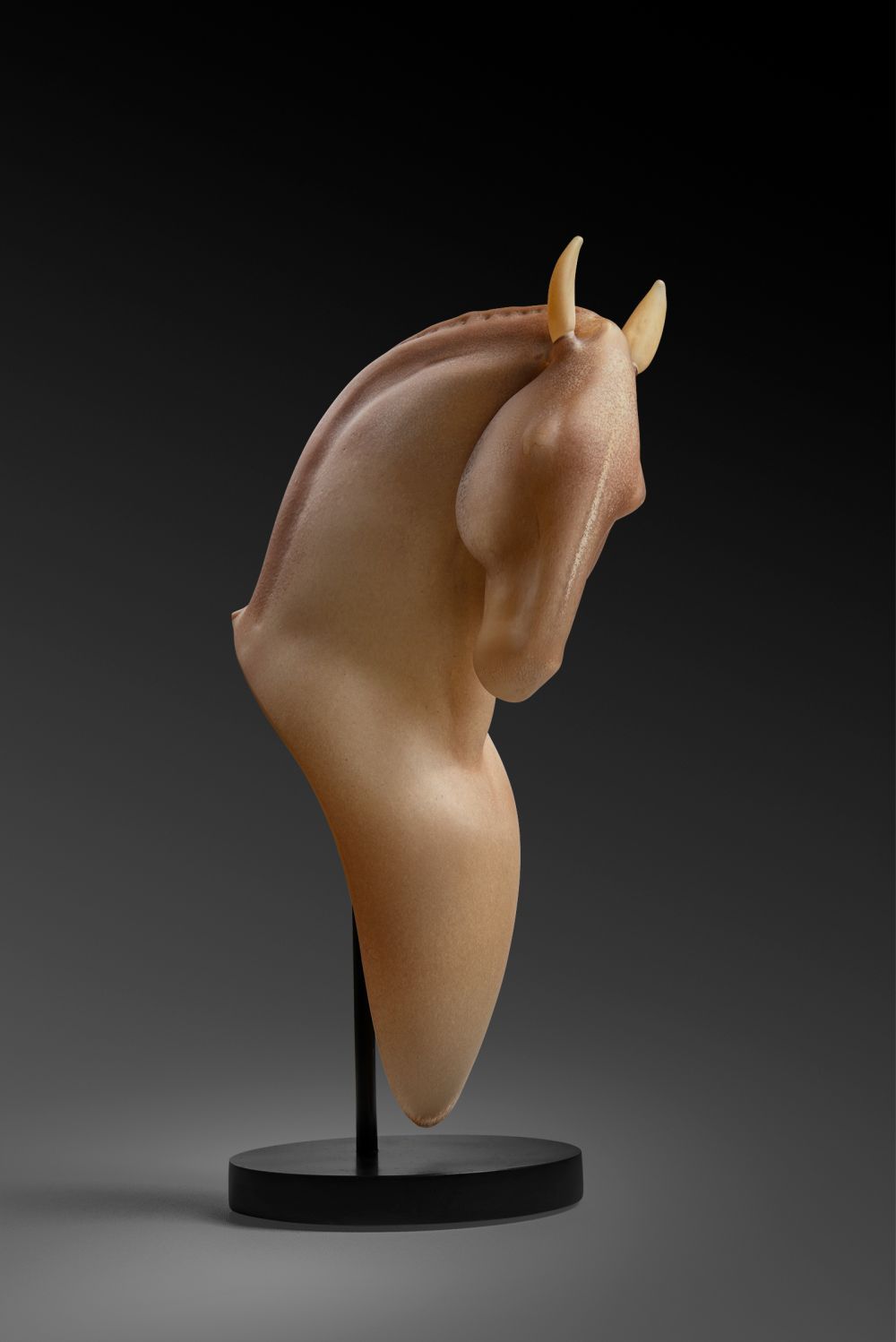 Sculpted horse head, beige tone, on black stand, against a dark gray background.