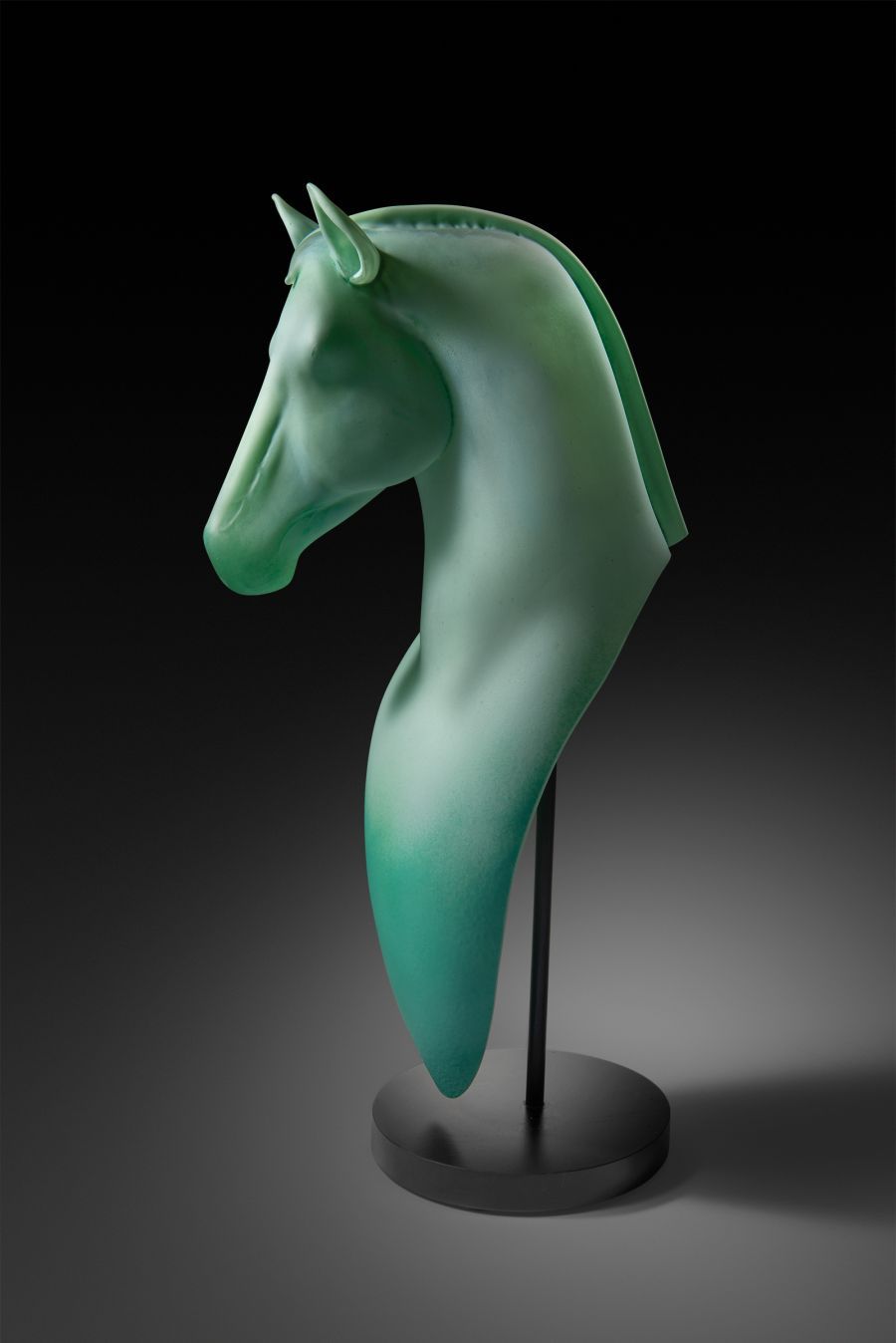 Green glass horse head sculpture on black stand.