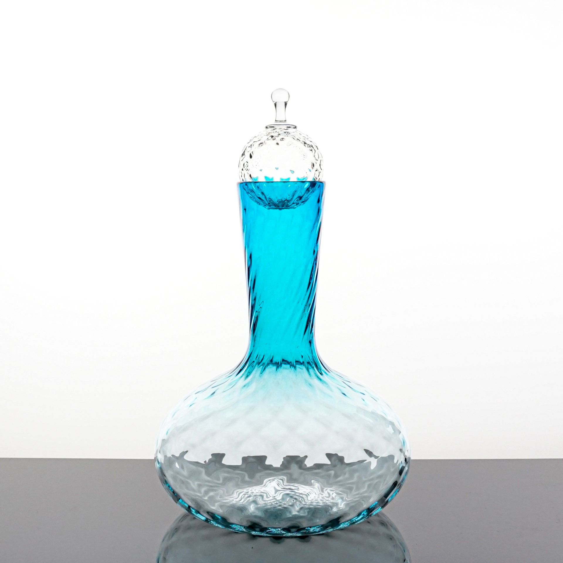 Blue glass carafe with a bulbous base, a tall, twisted neck, and a decorative stopper, filled with blue liquid.