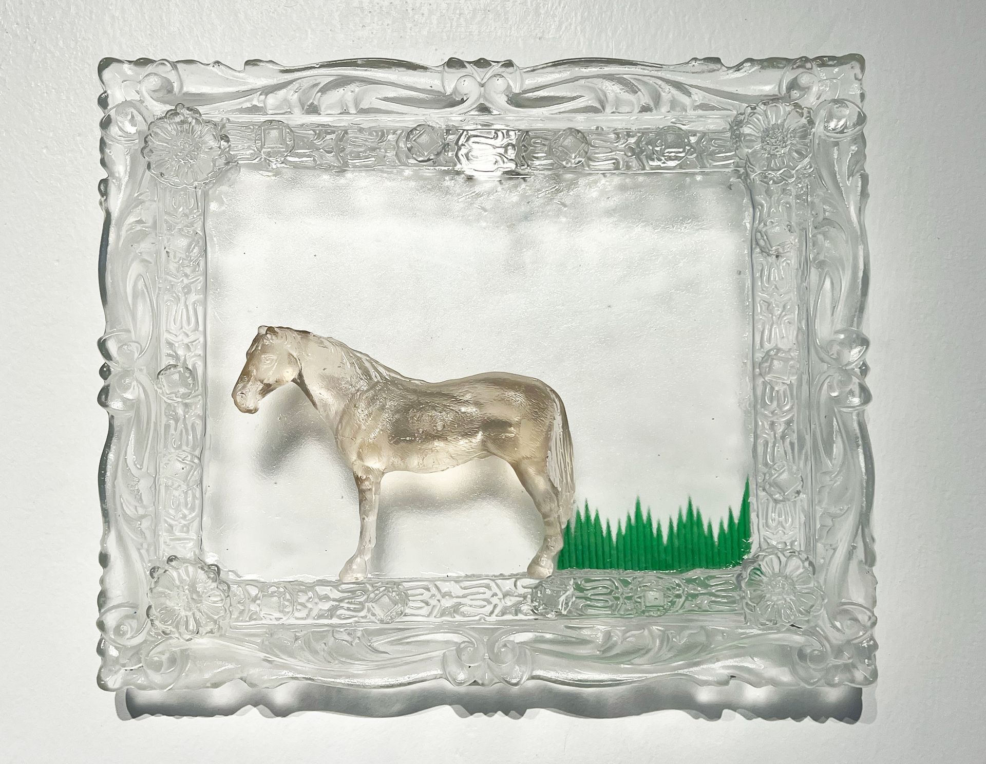 Clear, ornate glass frame with a translucent horse and green grass.