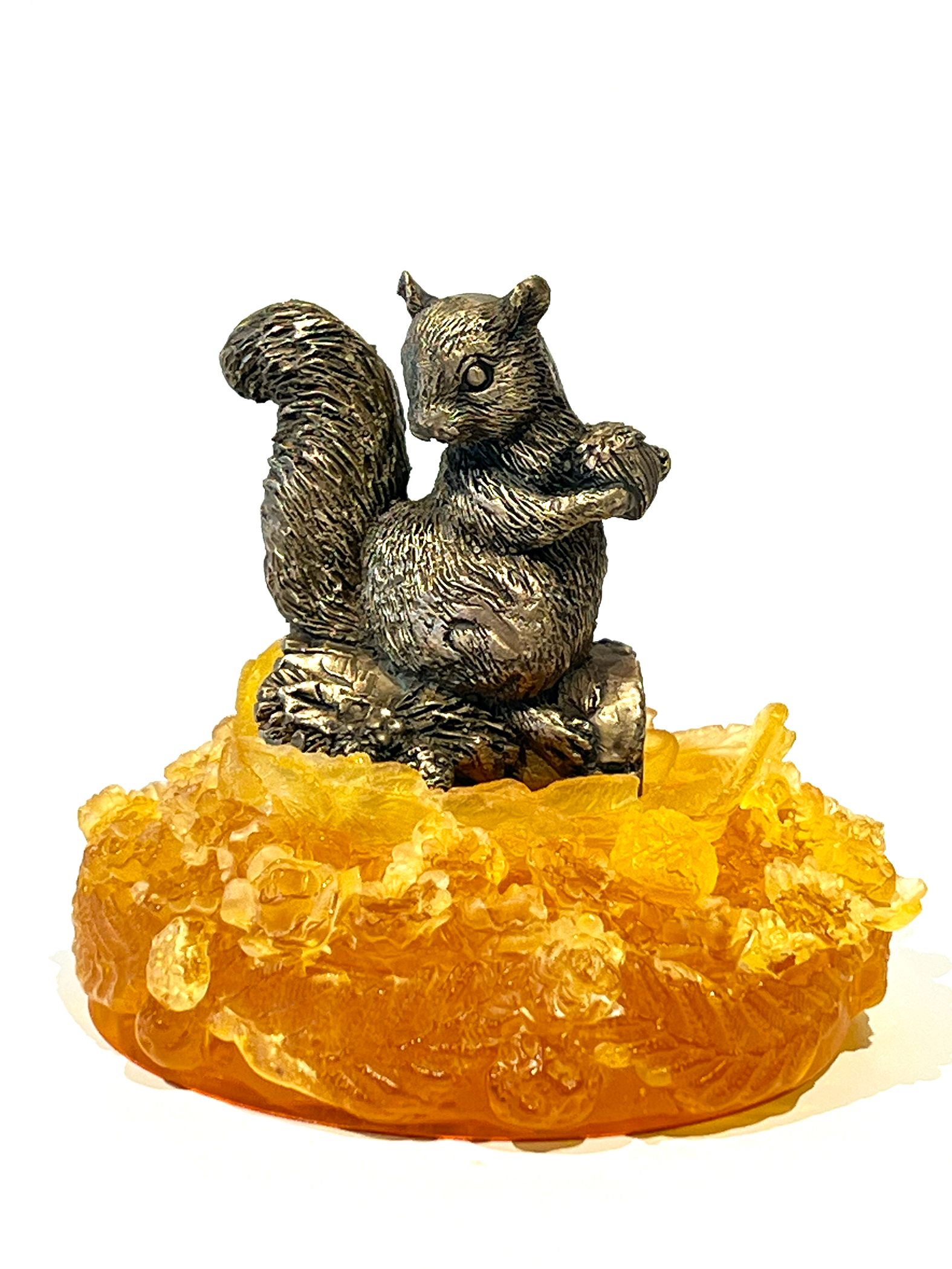 Squirrel statue perched on a yellow, amber-like base, holding a nut.