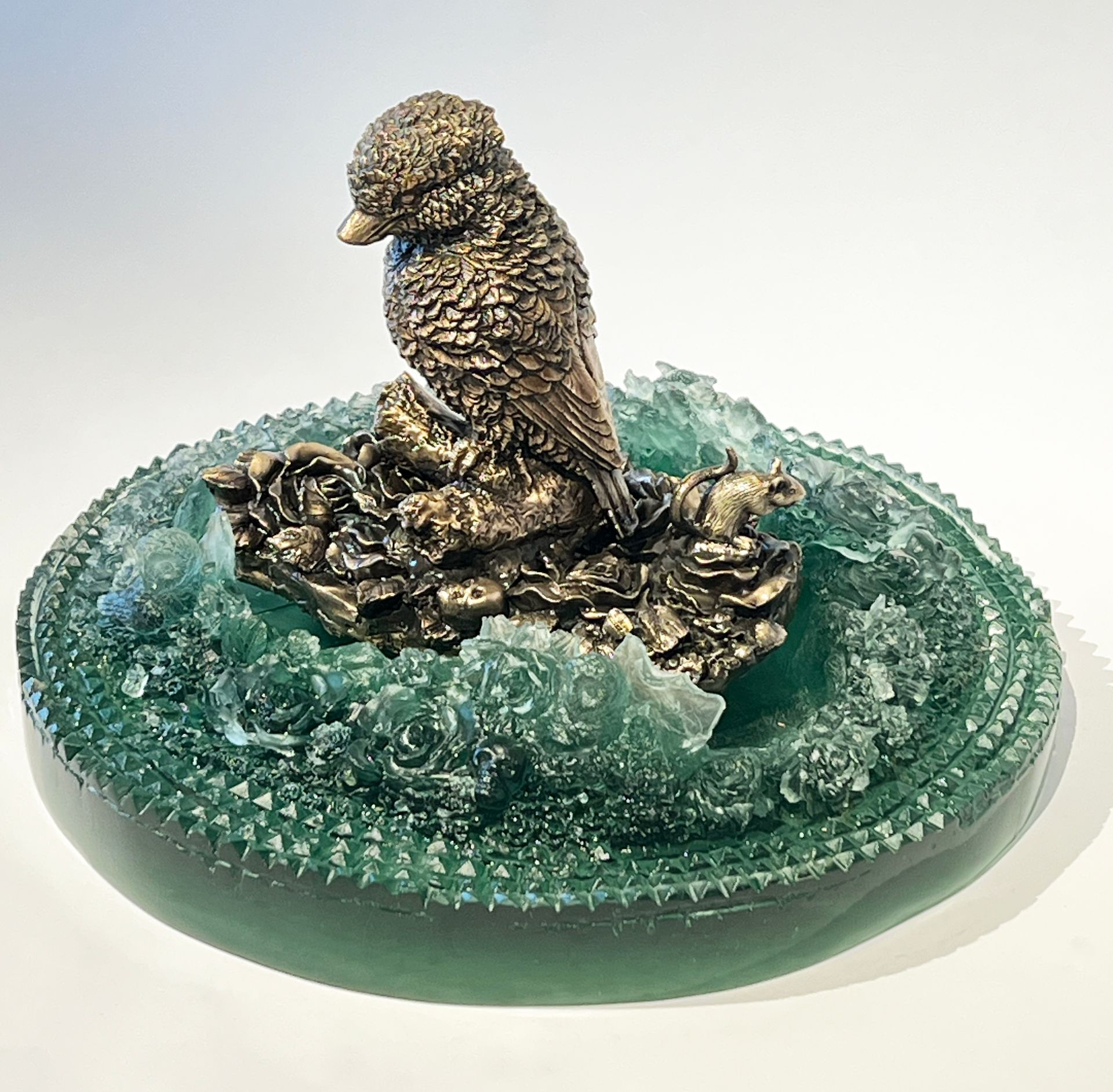 Bronze bird sculpture atop green glass wave on a round base.