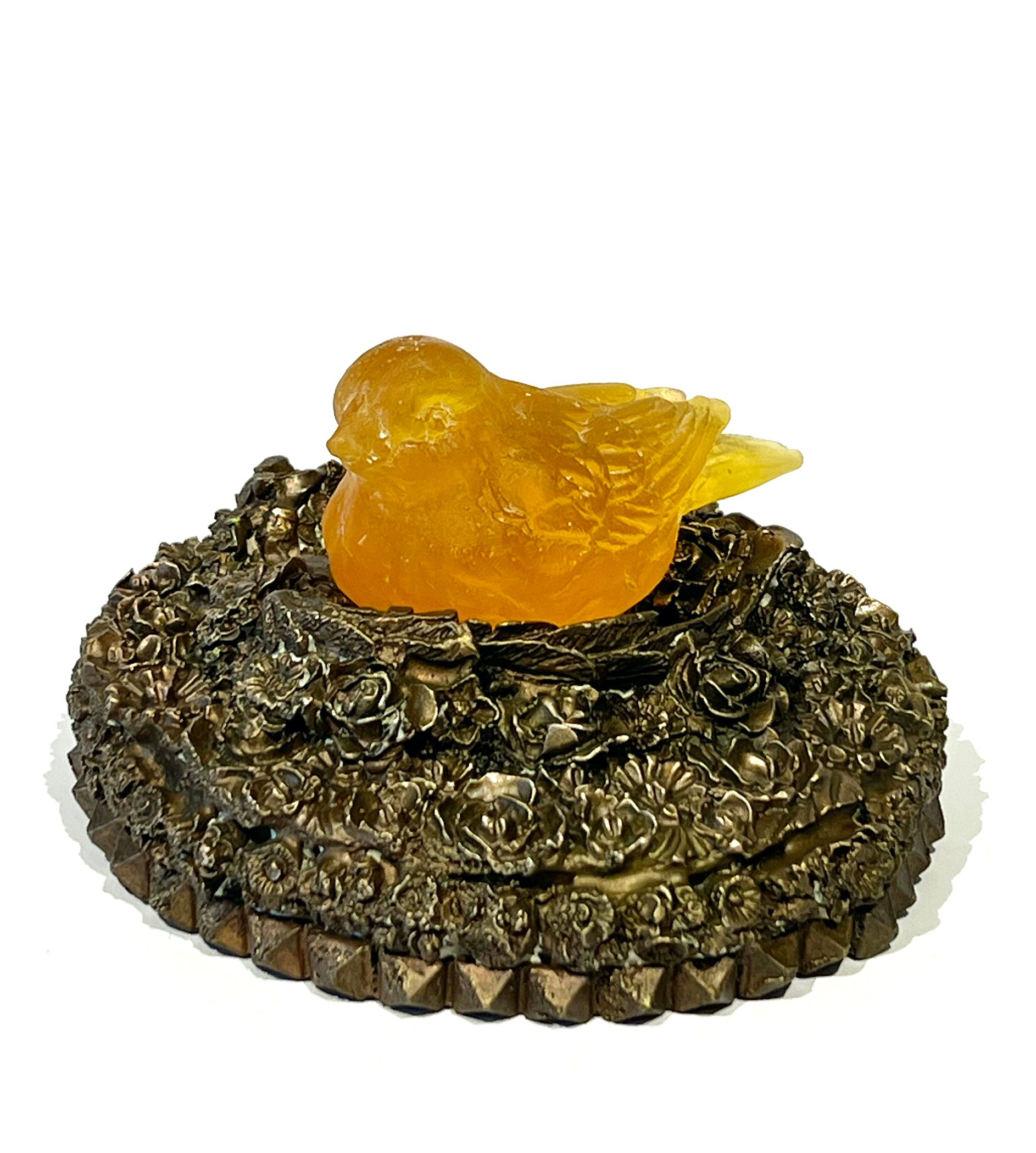 Amber bird figurine on a bronze-toned, ornate nest-shaped box.
