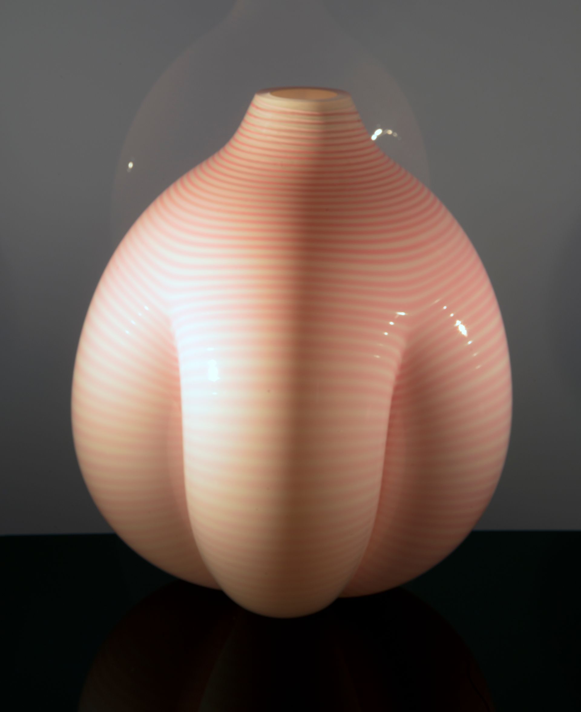 Pink, bulbous ceramic vase with horizontal stripes and three curved lobes, on a black surface.