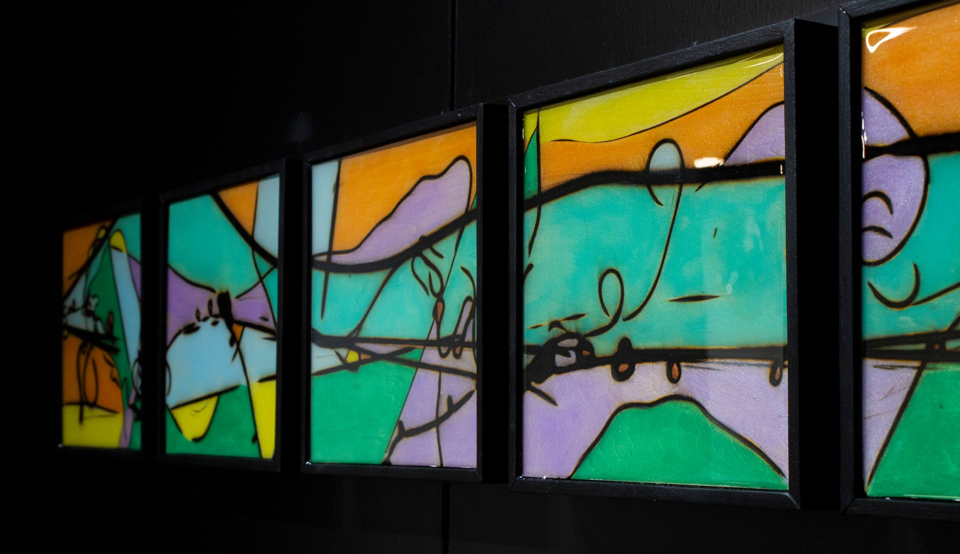 Abstract art: framed panels with colorful geometric shapes and black lines against a dark background.