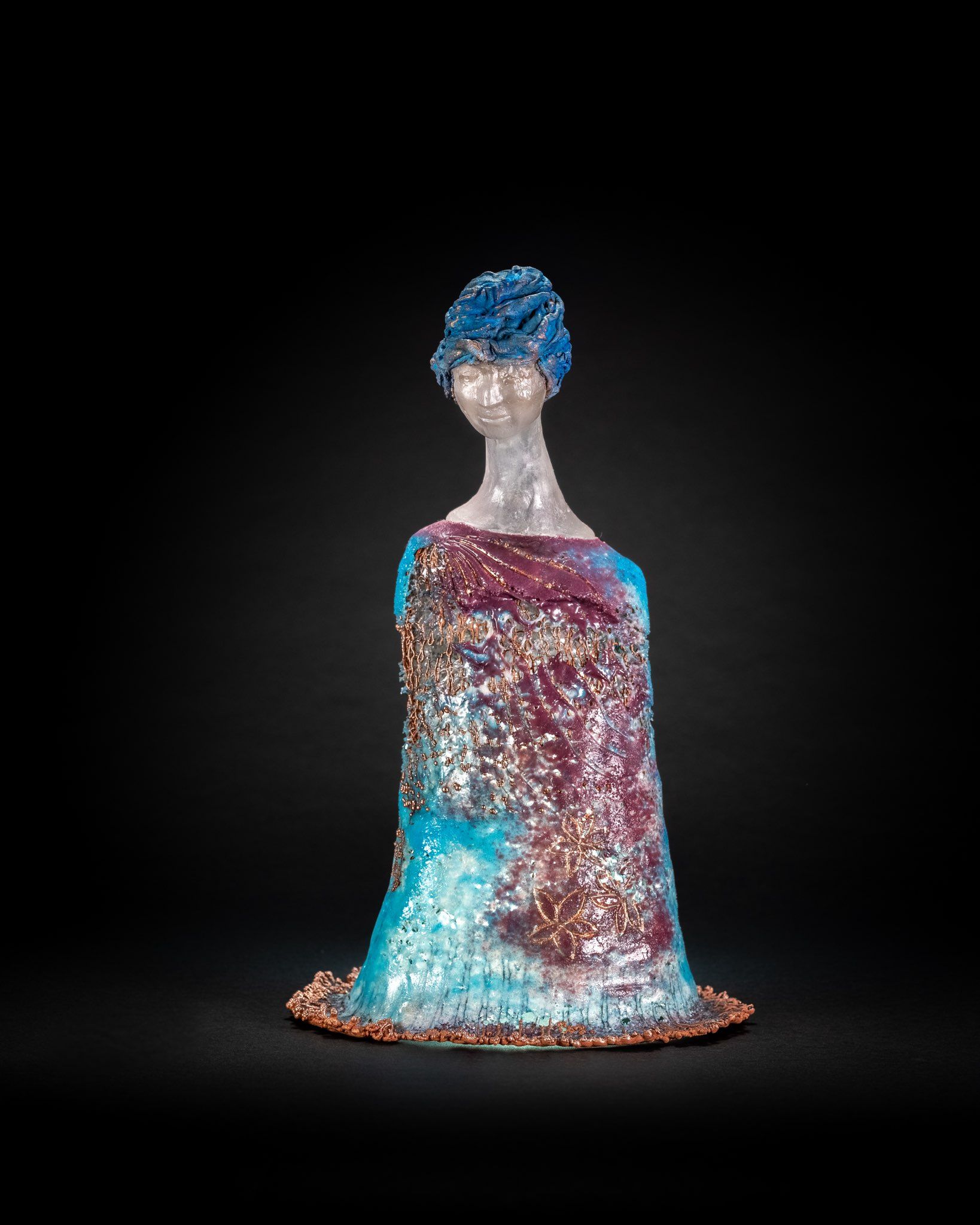 Sculpture of a slender figure in a blue and burgundy dress, with a blue textured hairstyle, on a black background.