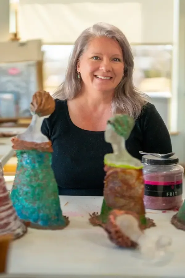 Woman smiling next to colorful sculptures. Bright workshop, smiling.