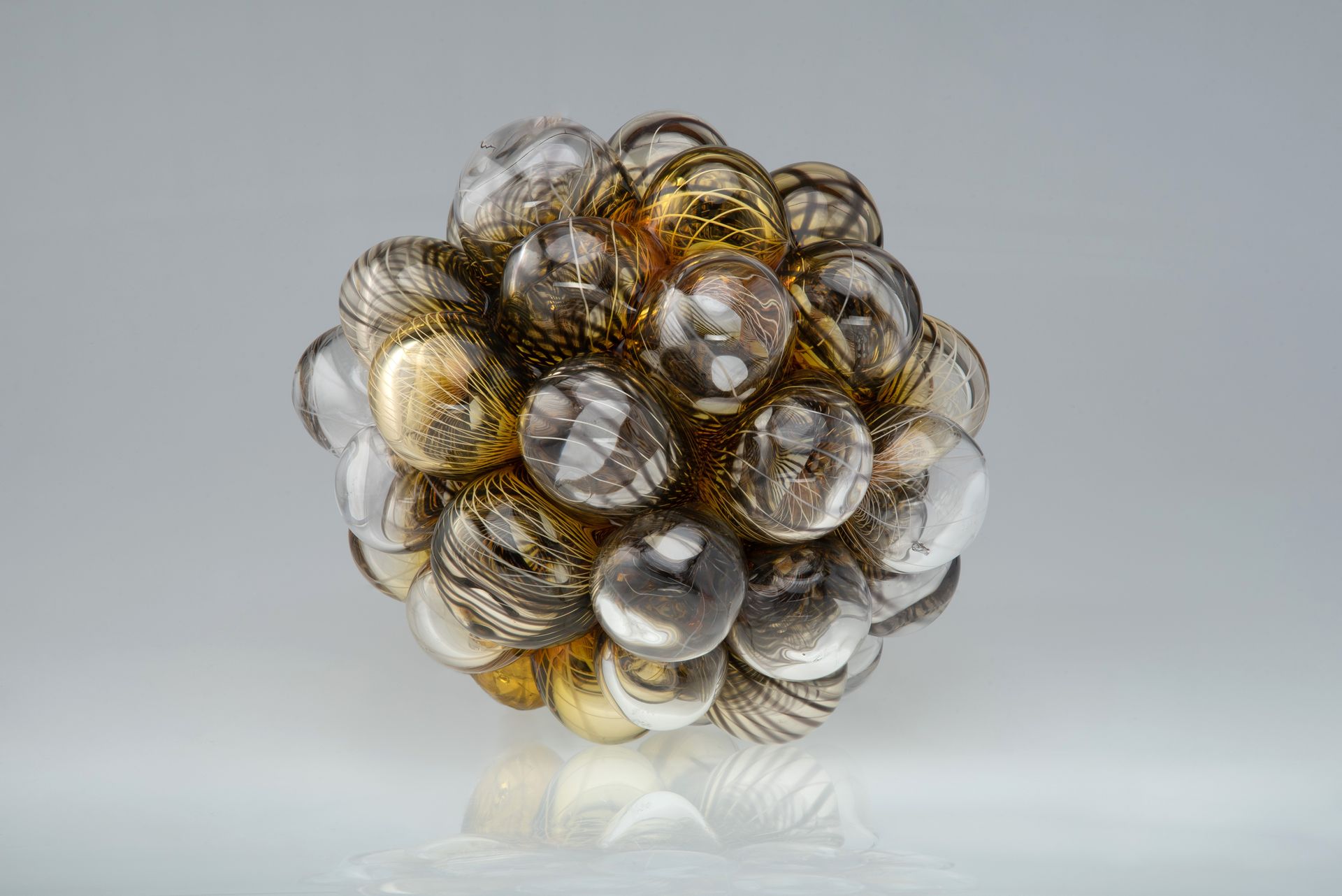 Cluster of glass spheres in gold, silver, and clear, arranged on a reflective surface.