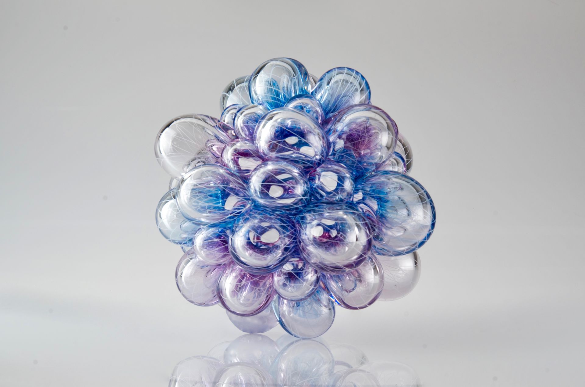 Glass sculpture of a cluster of blue and purple bubbles, reflecting light on a white surface.