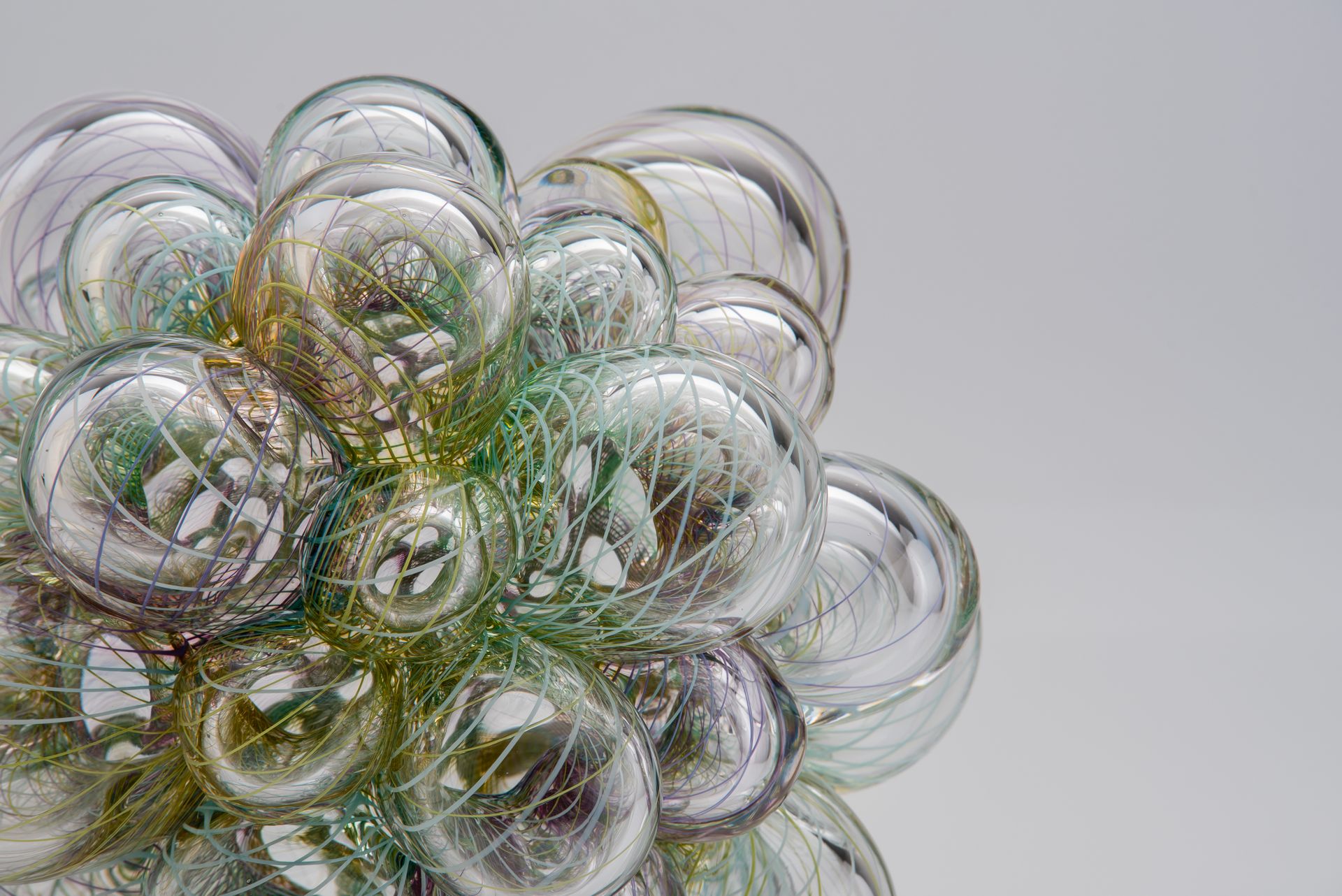 Cluster of clear, iridescent glass bubbles, some reflecting green and gold light, on a white background.