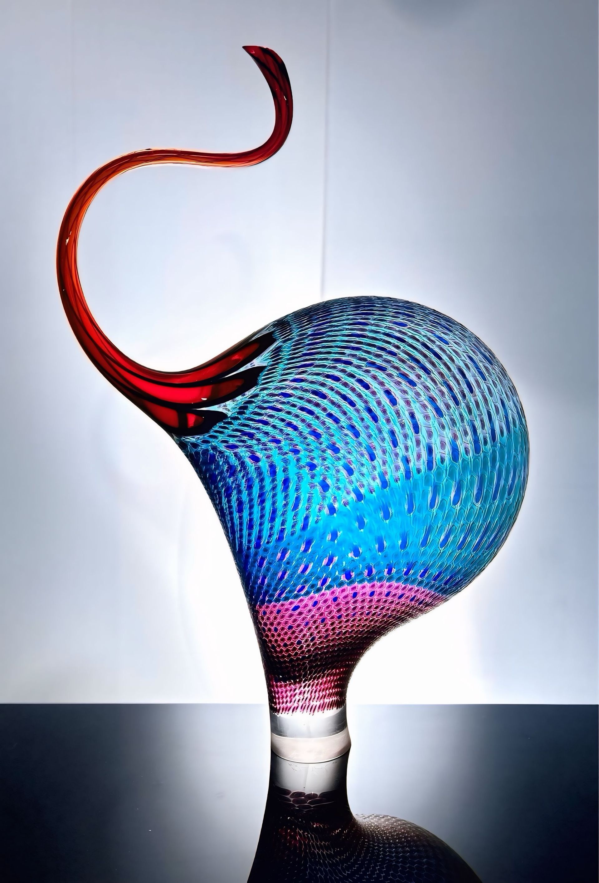 Glass sculpture in shades of blue, red, and purple, with a long, curved neck and bulbous body.