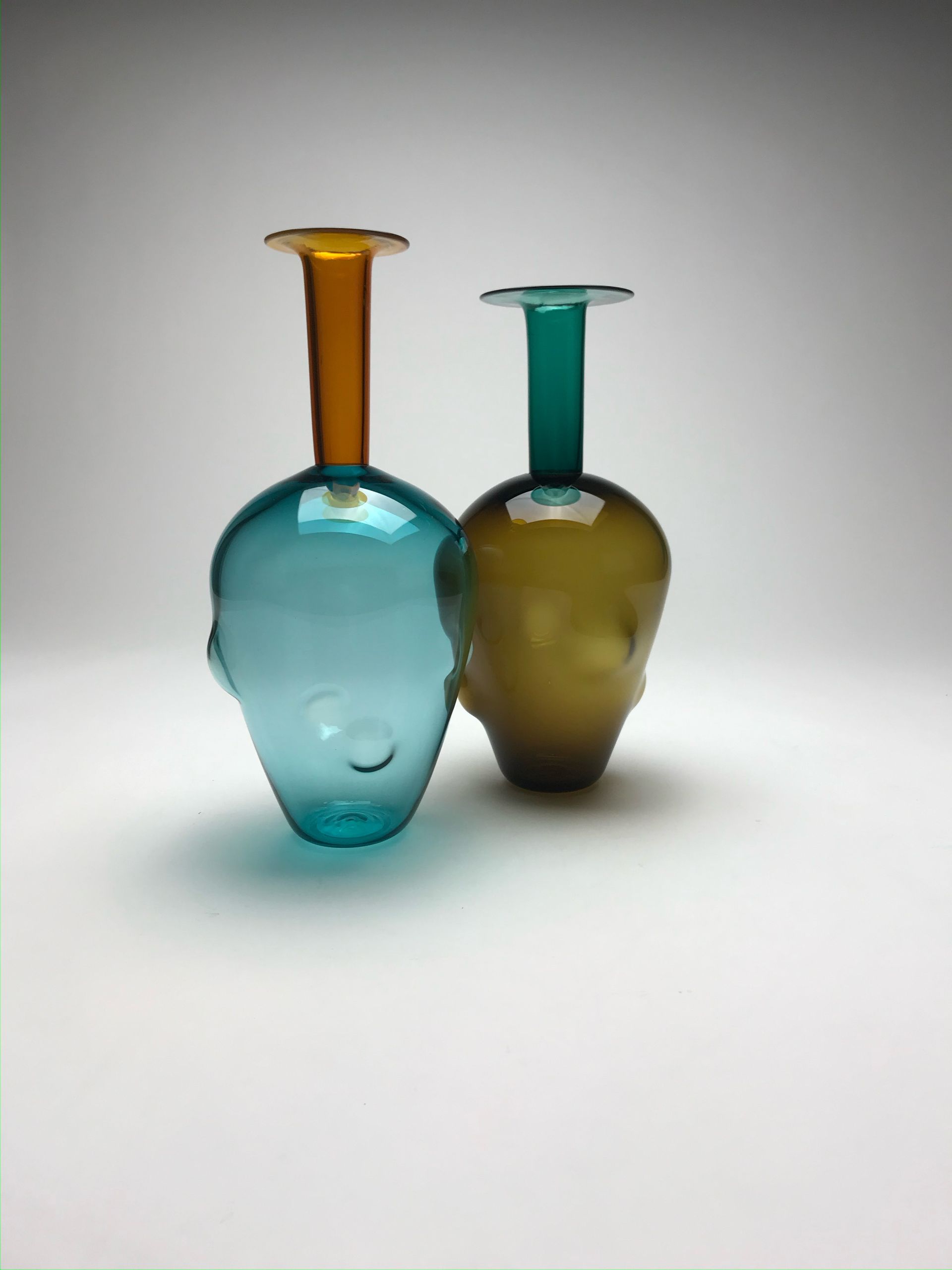 Two colorful glass vases, one blue and gold, the other green and brown, stand on a white surface.