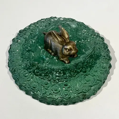 Bronze rabbit sculpture inside a green glass dish with floral pattern.