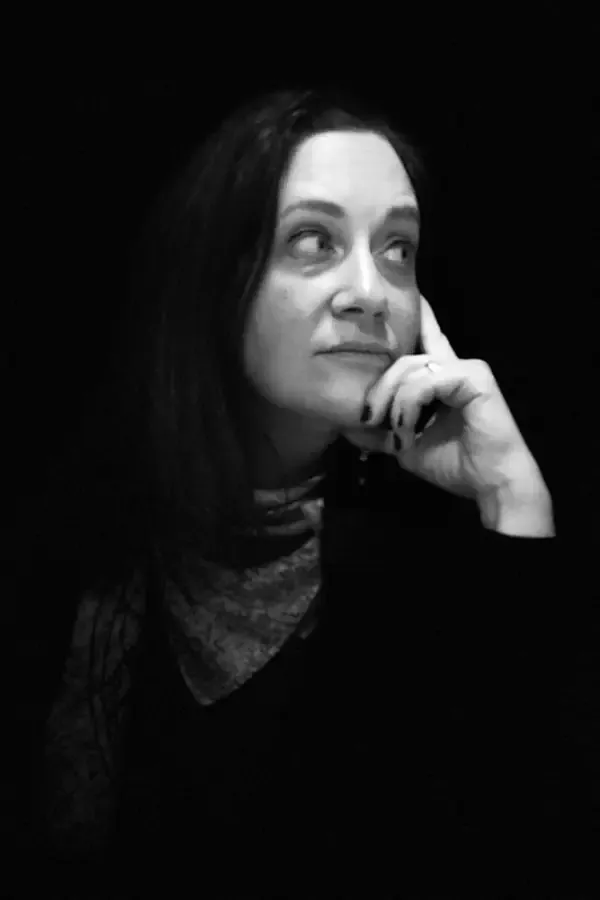 Woman in black and white, head tilted, hand on chin, looking upwards, thoughtful expression.