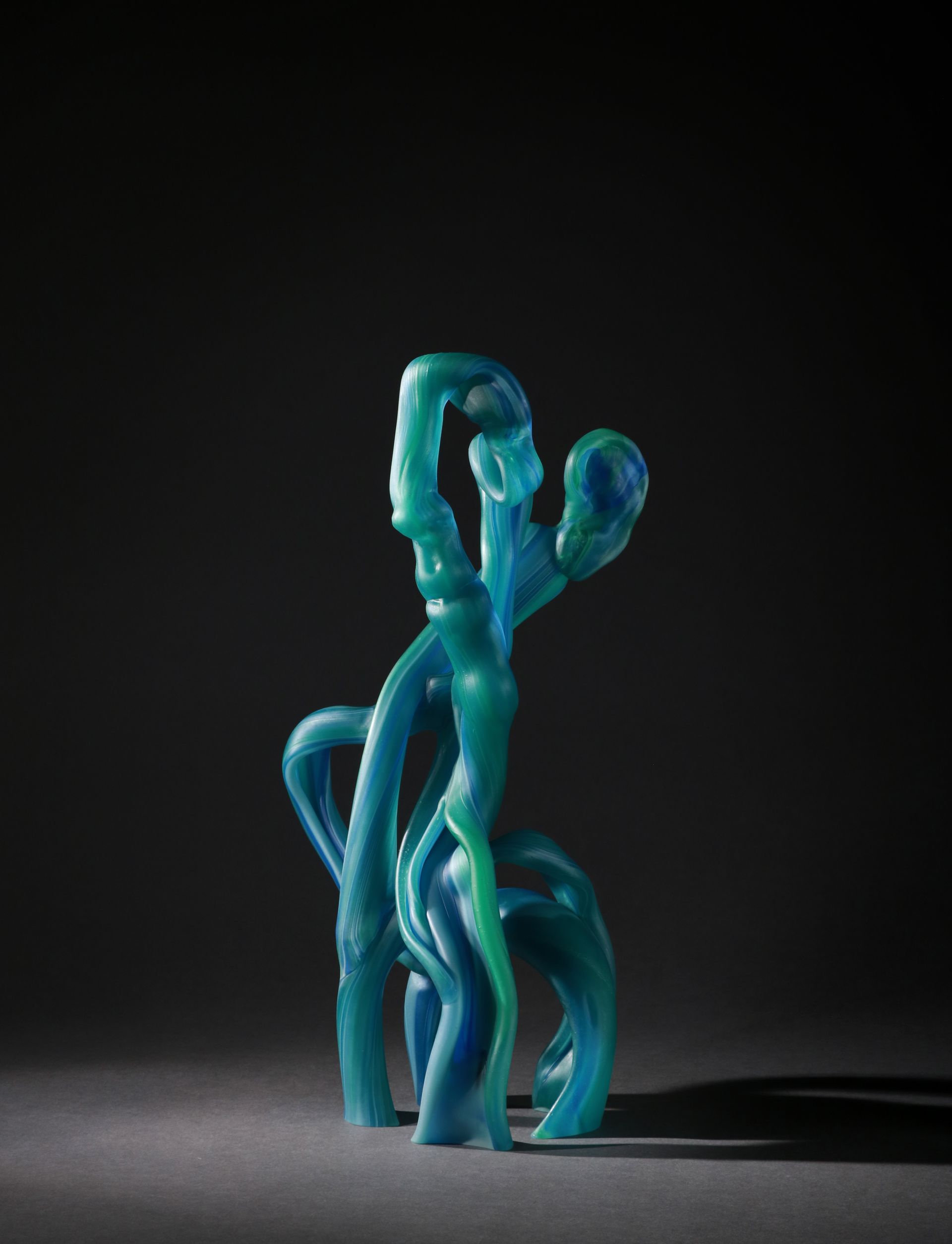 Abstract blue and green glass sculpture on a dark background. Twisted, organic shapes.