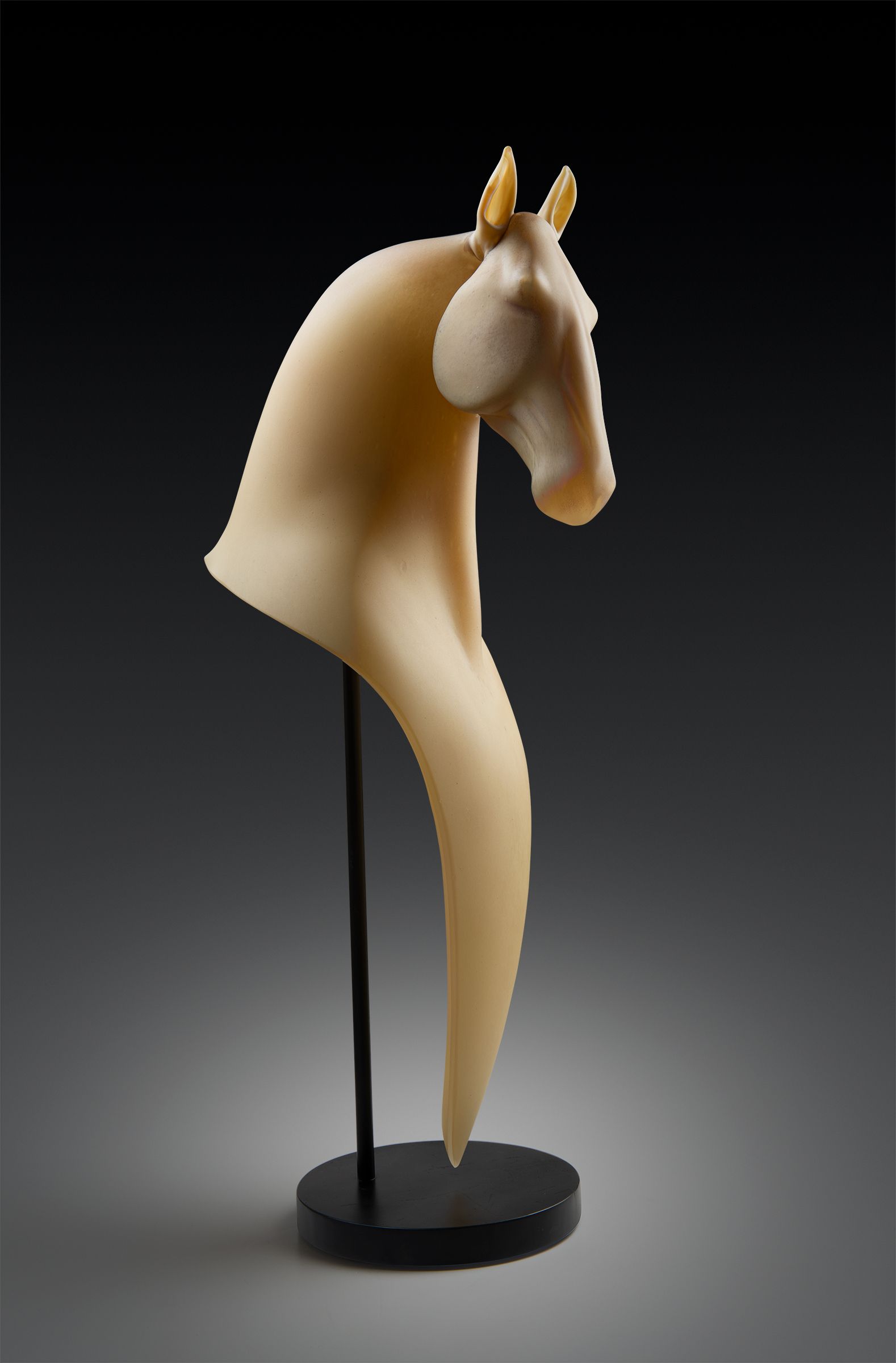 Sculpture of a horse's head and neck, cream-colored, supported by a thin black rod on a black base against a dark backdrop.