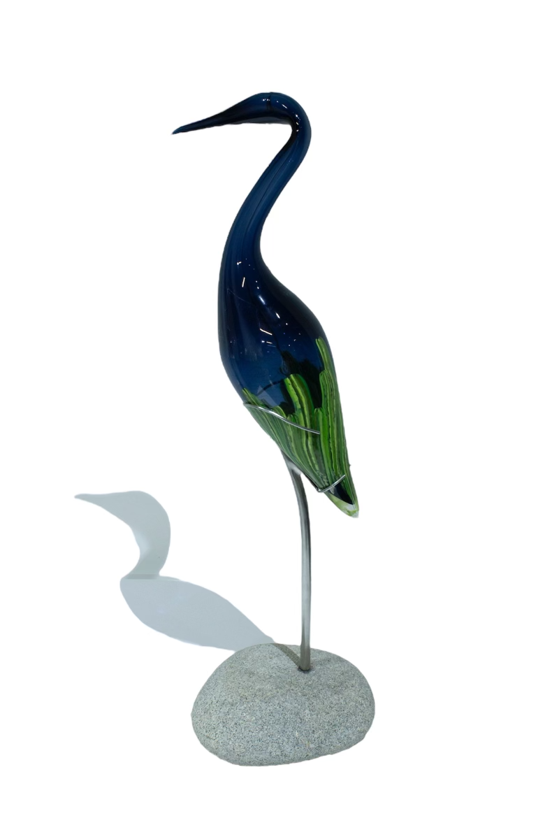 Glass heron sculpture with dark blue body and green accents, standing on a rock.
