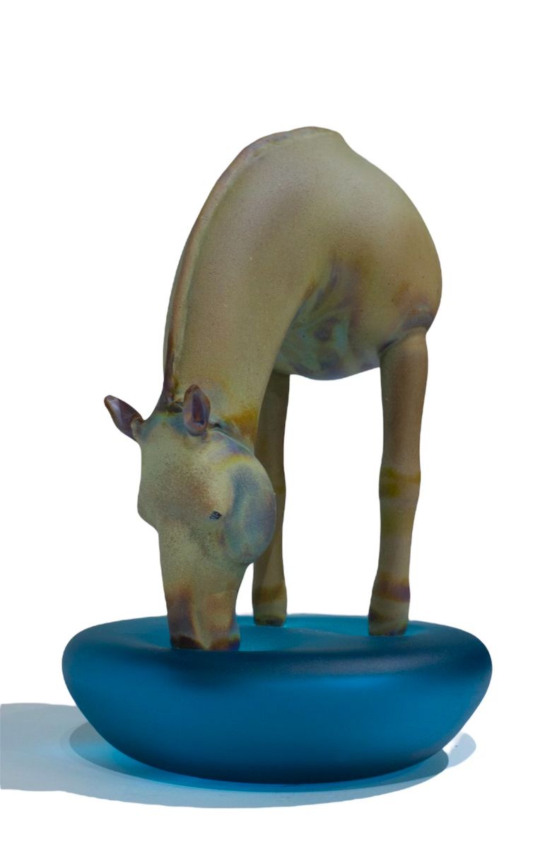 Horse figurine drinking from a blue bowl.