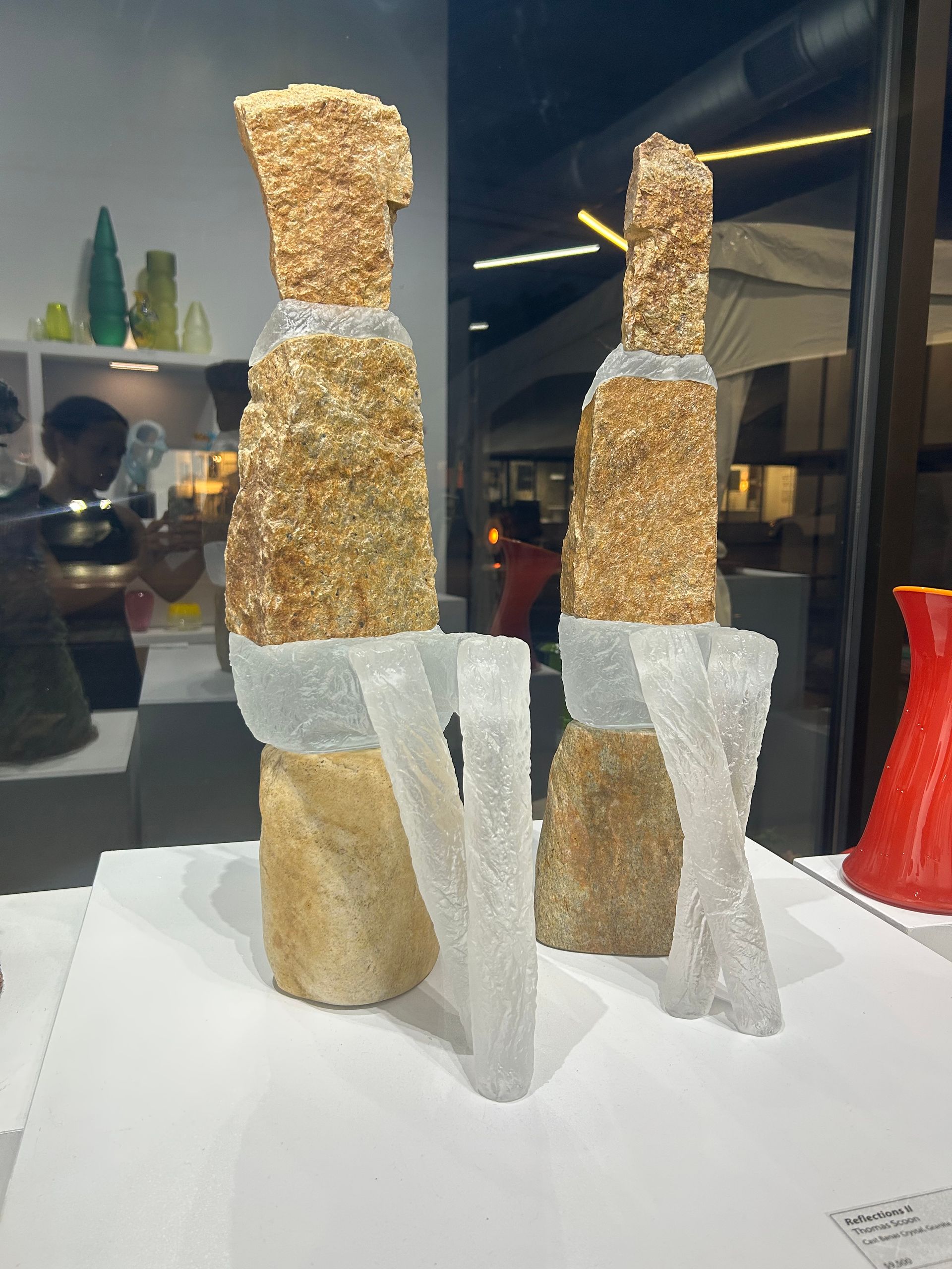 Two abstract sculptures made of tan, rough material, with transparent, geometric legs.