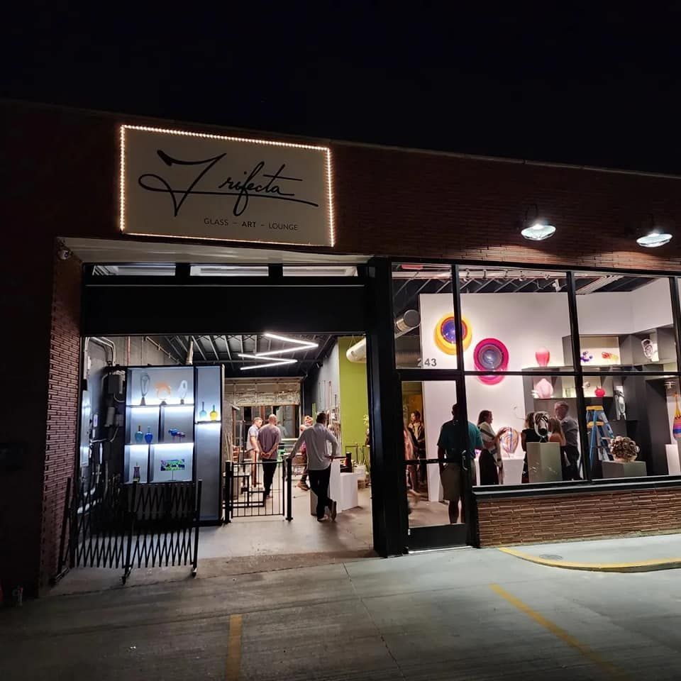 Night view of an art gallery, Zinfante, with people inside looking at art. Storefront with lights and sign.
