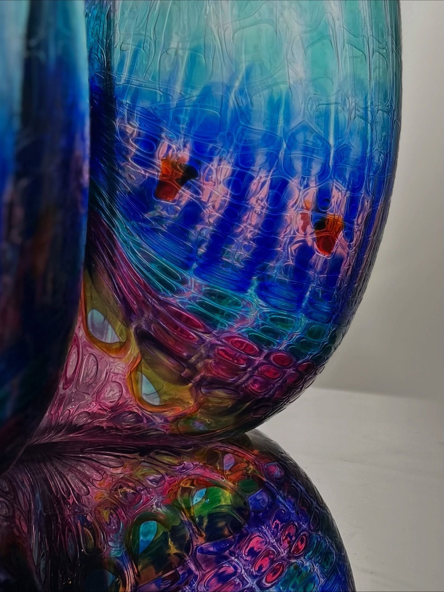 Close-up of a vibrant, layered glass art piece in blues, pinks, and greens, with reflective surface.