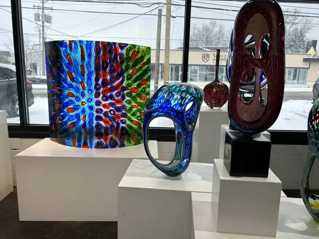 Glass sculptures on white pedestals in a gallery with a snowy window backdrop.