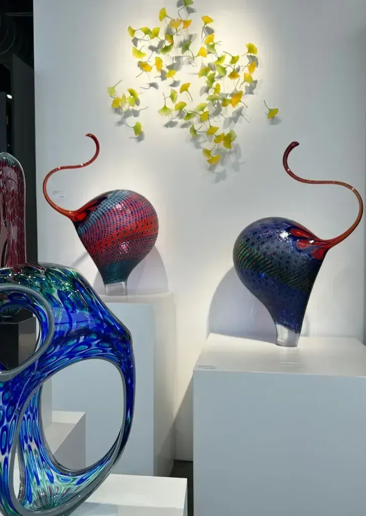 Glass art display: colorful orb sculptures with curved red tendrils, white wall with yellow leaf art.