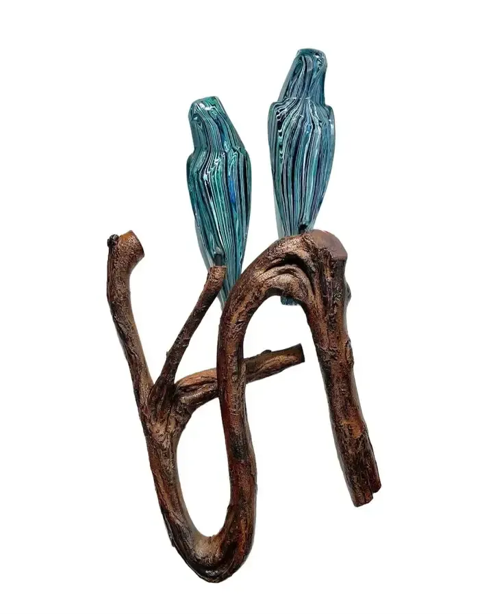 Two teal-colored bird sculptures perch on a brown, twisting branch against a white background.