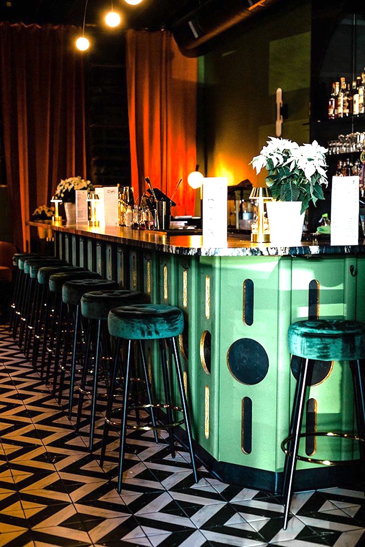 Green bar with velvet stools and black and white tiled floor.
