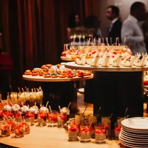 Buffet table with appetizers and drinks at an event, with people in the background.