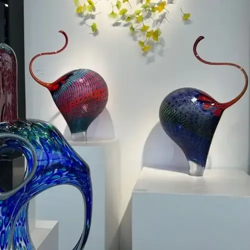Glass art display featuring colorful, abstract sculptures on white pedestals.