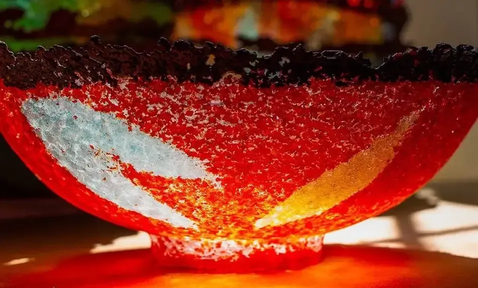 Red glass bowl with white and yellow accents, black rim, sitting on a red base.