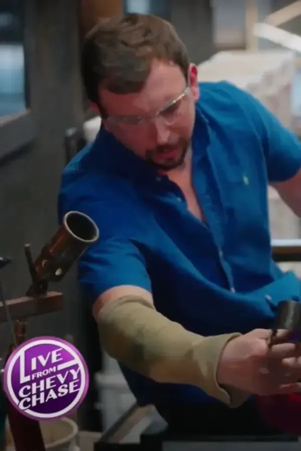 Man in blue shirt, safety glasses, and arm sleeve working with glass in a workshop.