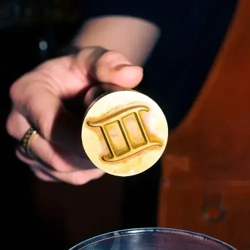 Hand holding a circular brass stamp with the roman numeral 3 symbol.