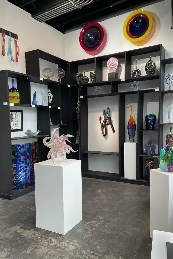 Art gallery with glass sculptures on pedestals and shelves; colorful, modern art.